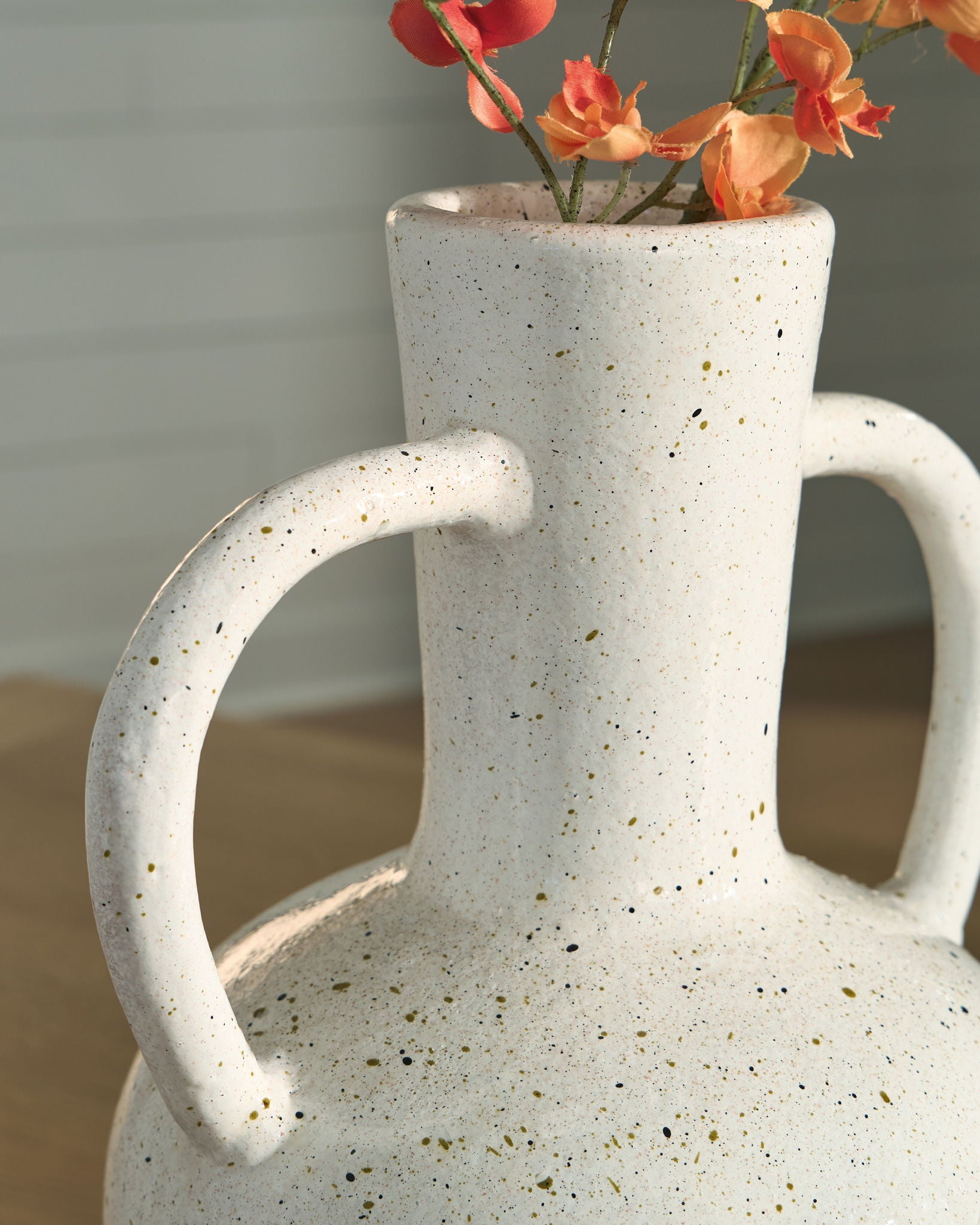 Speckled white ceramic vase with red flowers and two loop handles.
