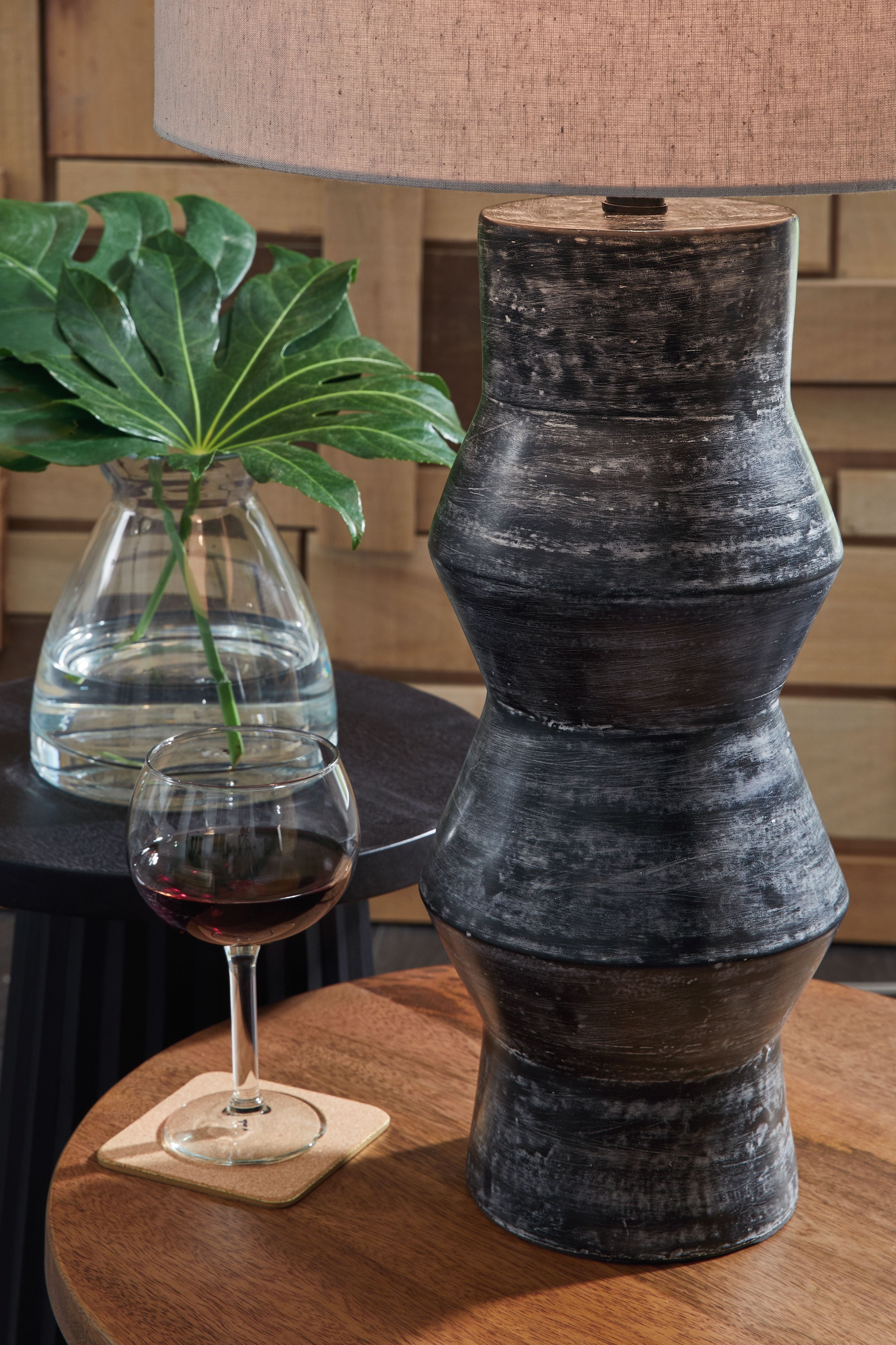 Distressed black table lamp with beige drum shade and stacked vase-style base.