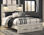 Light wood bed with plaid comforter and black bar handles on the storage drawer base