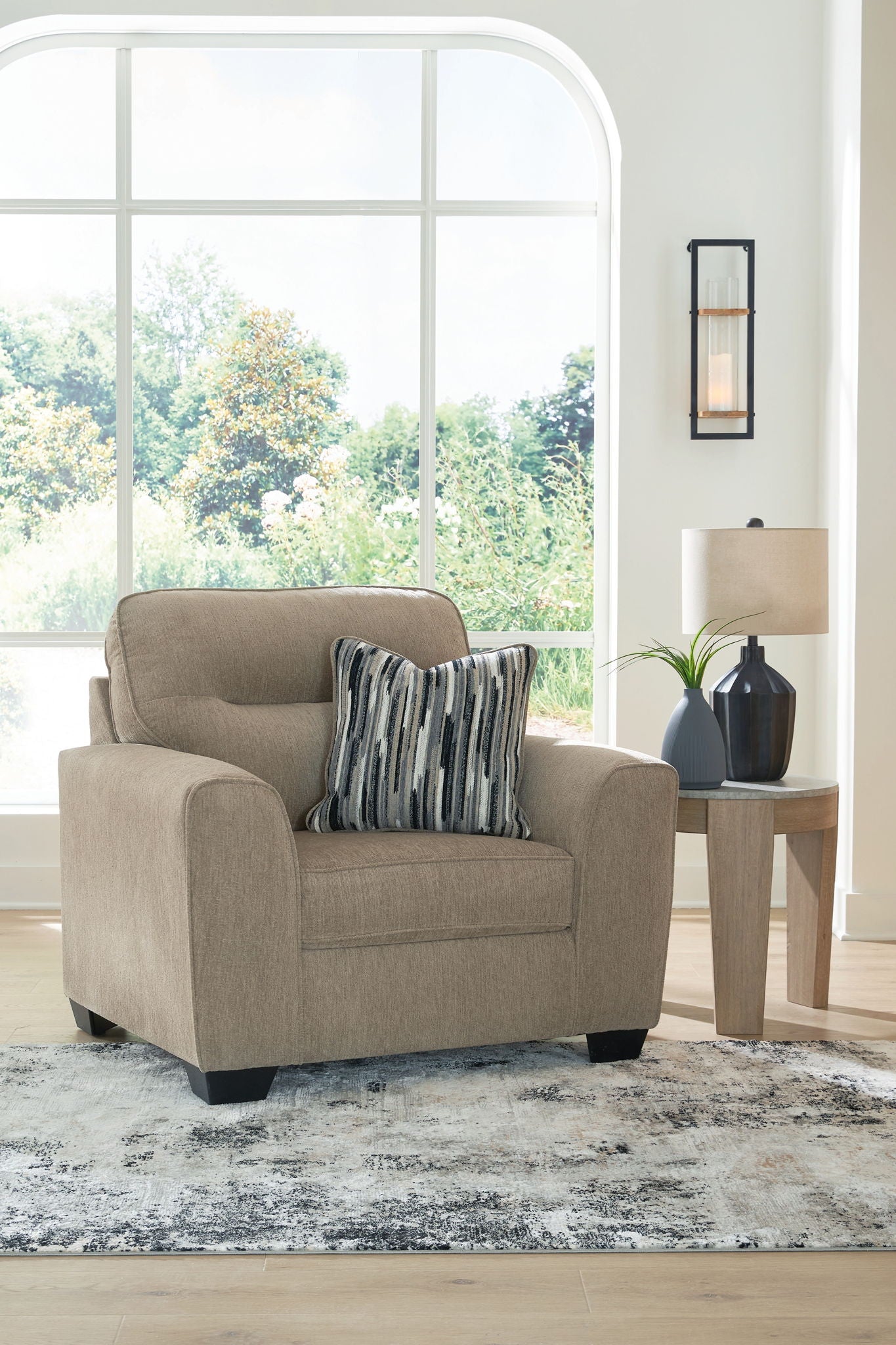 Light brown upholstered chair and a half with striped throw pillow and rounded arms
