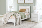 White panel platform bed with scalloped headboard, layered bedding and decorative pillows