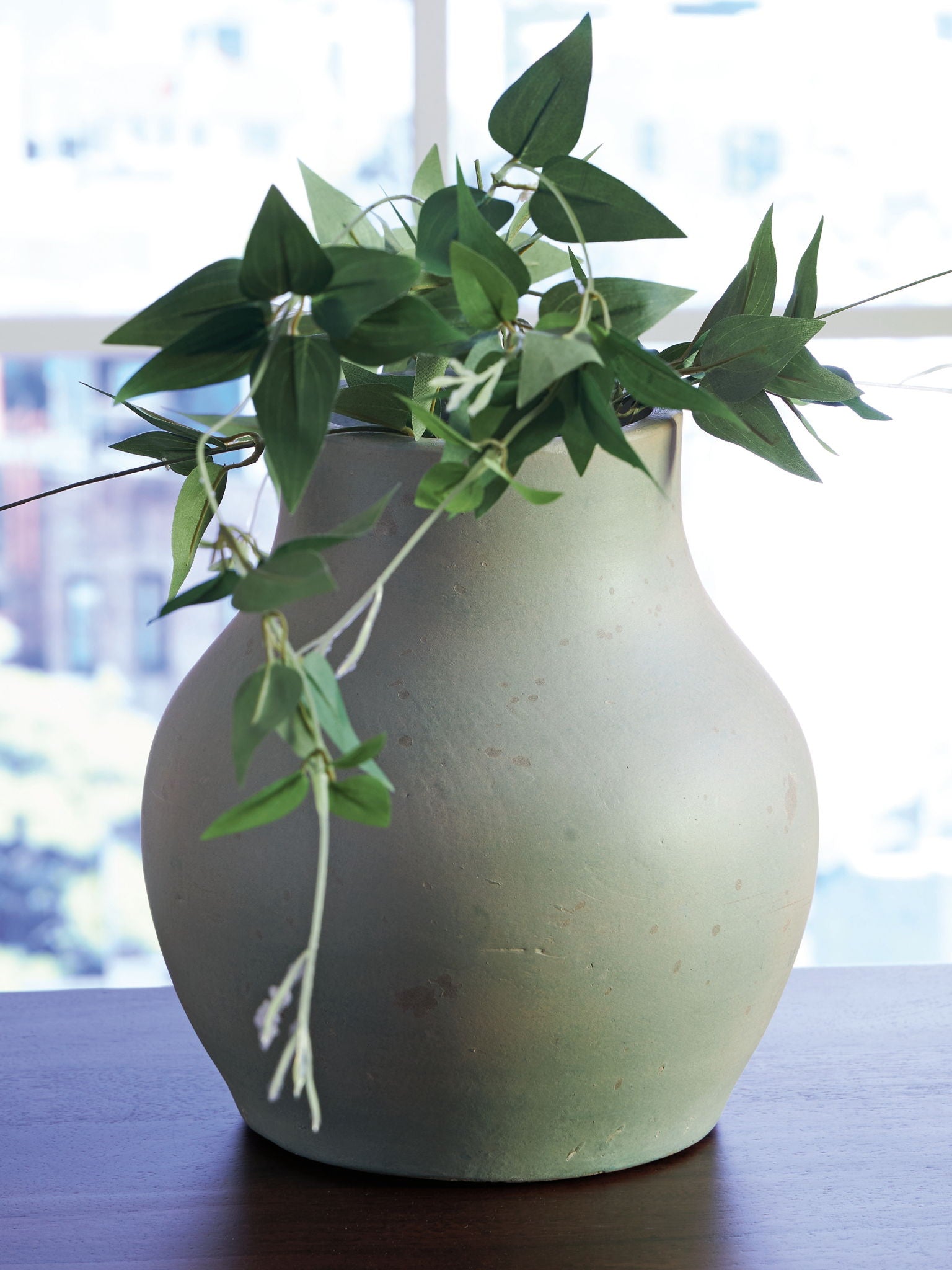 Green ceramic vase with stems and leaves arrangement in the opening