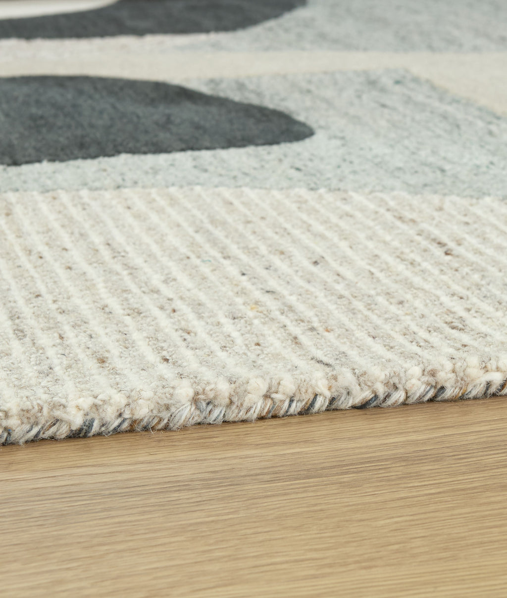 Close-up beige area rug showing textured pile with wavy concentric lines and dark gray shape