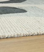 Close-up beige area rug showing textured pile with wavy concentric lines and dark gray shape