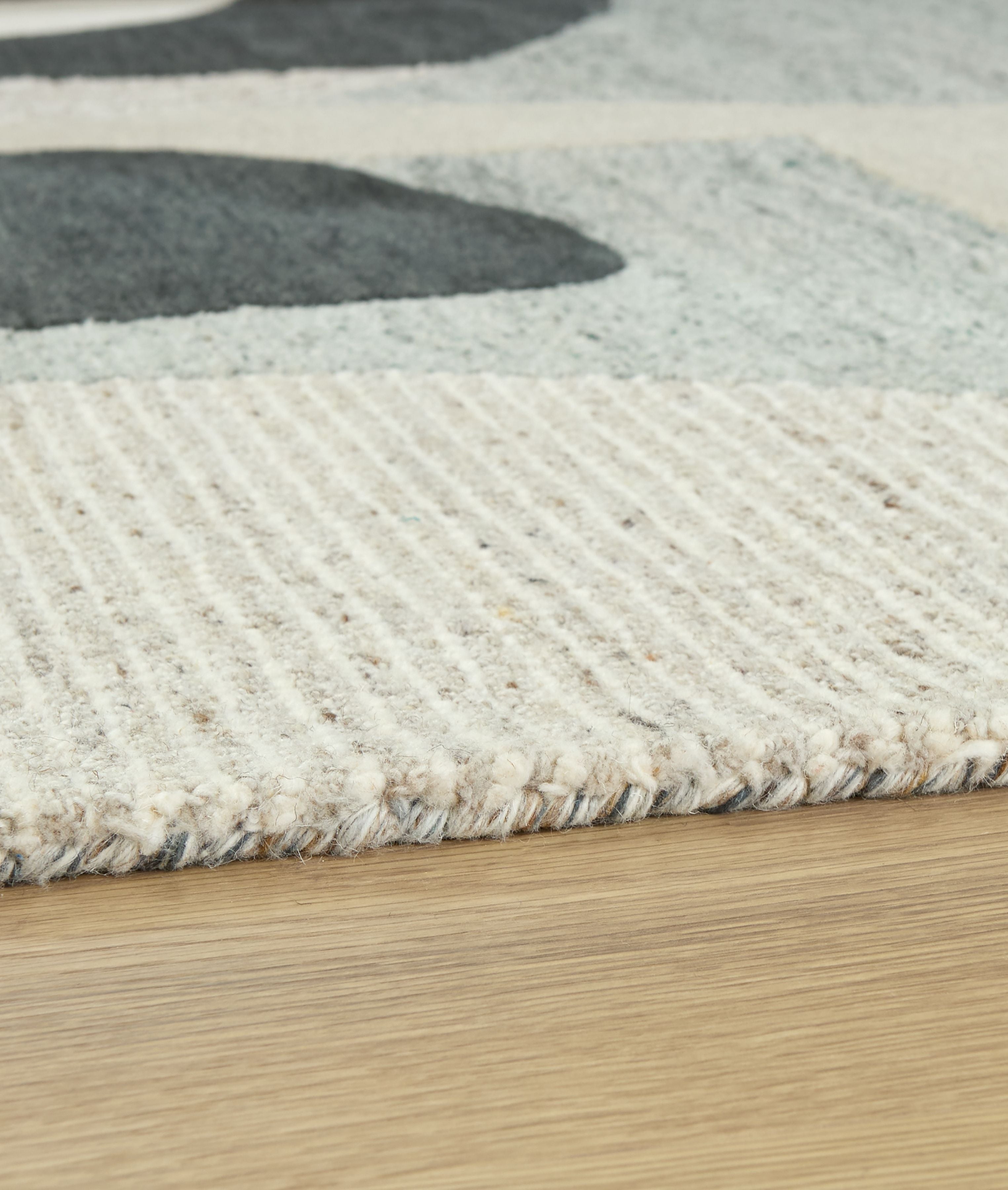 Close-up beige area rug showing textured pile with wavy concentric lines and dark gray shape