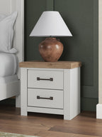 White two-drawer night stand with brown top and dark metal handles beside a lamp.