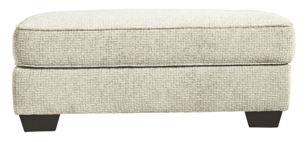 Sandstone upholstered ottoman with padded top and dark legs, side view