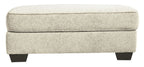 Sandstone upholstered ottoman with padded top and dark legs, side view