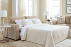 Sofa sleeper with bed extended, white bedding and striped throw, light tan frame