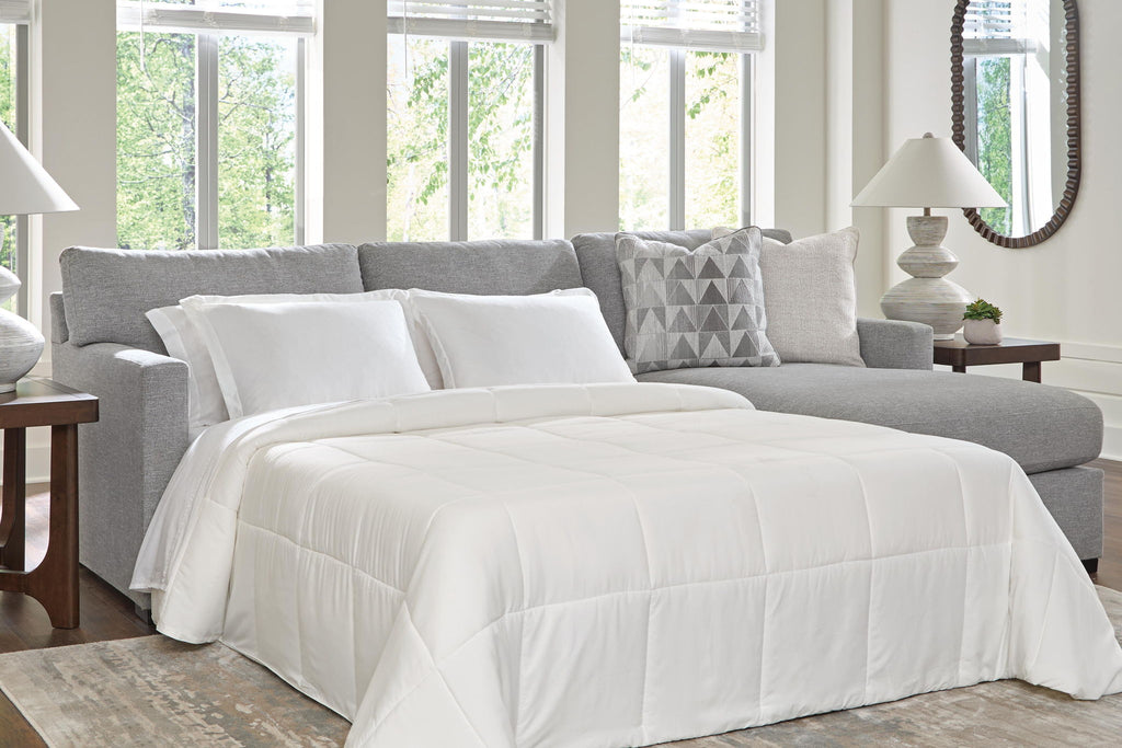 Dark gray sleeper sectional sofa with unfolded bed, white comforter, and geometric pillows