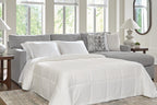 Dark gray sleeper sectional sofa with unfolded bed, white comforter, and geometric pillows