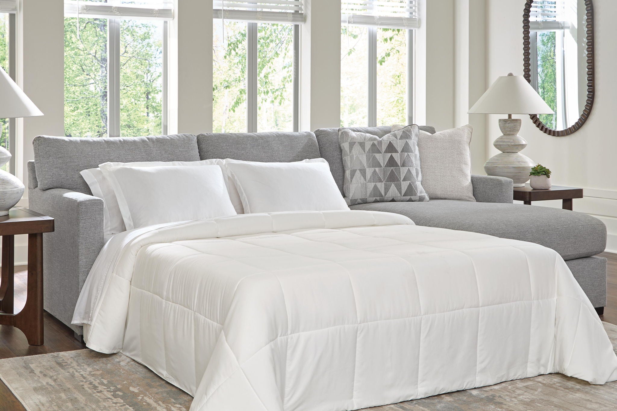 Dark gray sleeper sectional sofa with unfolded bed, white comforter, and geometric pillows