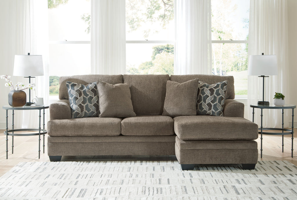 Taupe sofa chaise with two geometric patterned throw pillows in a living room setting