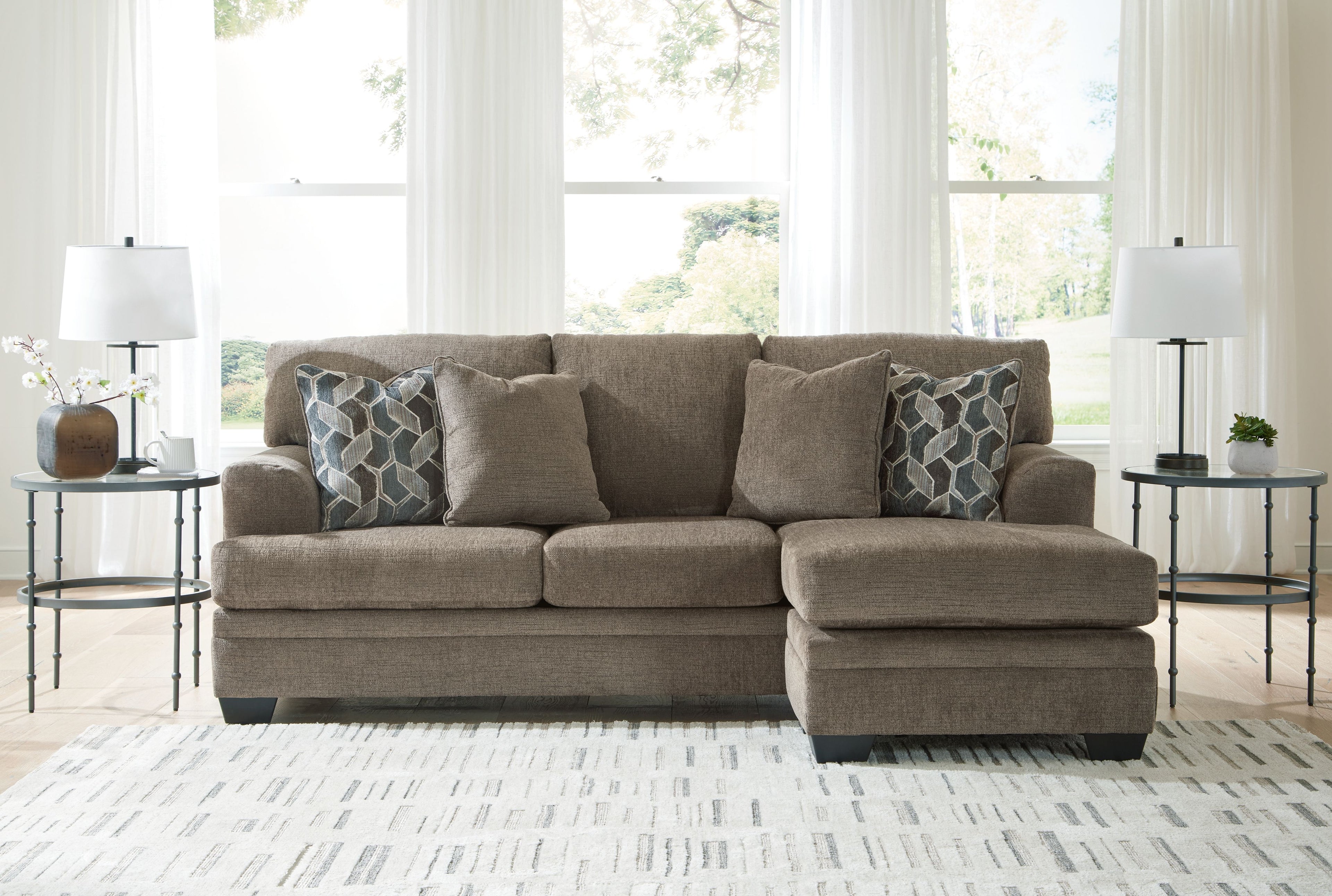 Taupe sofa chaise with two geometric patterned throw pillows in a living room setting