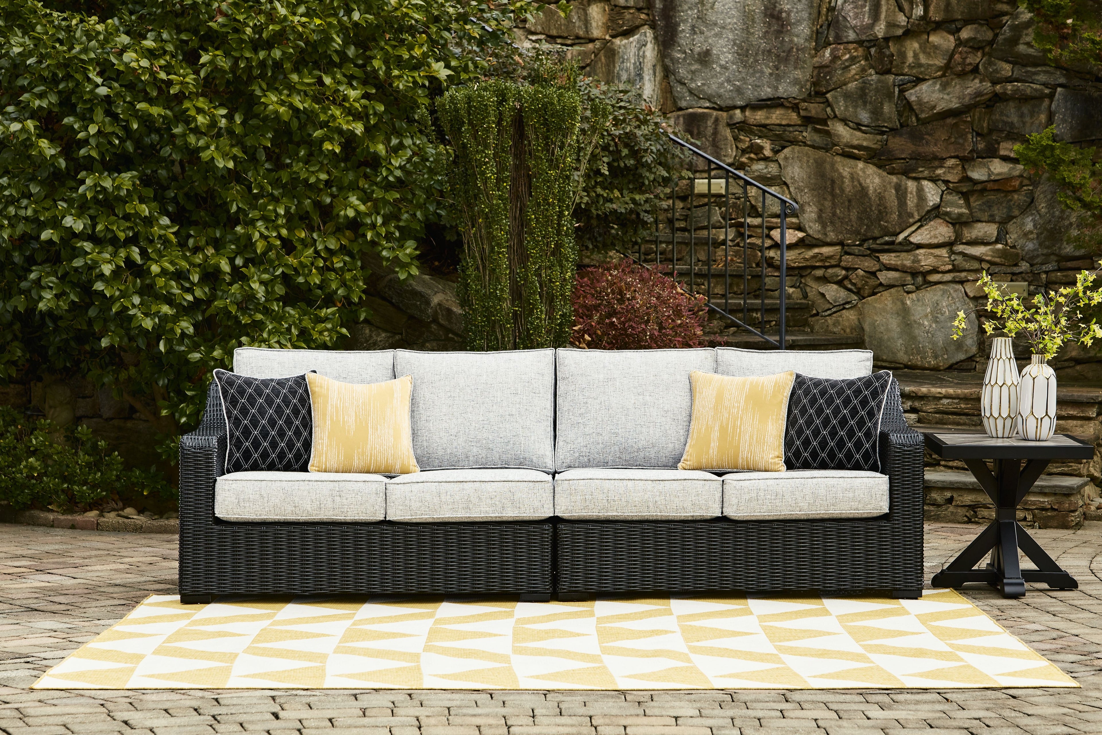 Outdoor loveseat with light gray cushions and black wicker base, yellow and patterned pillows