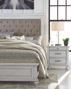 Upholstered bed side with beige tufted headboard and white nightstand with lamp