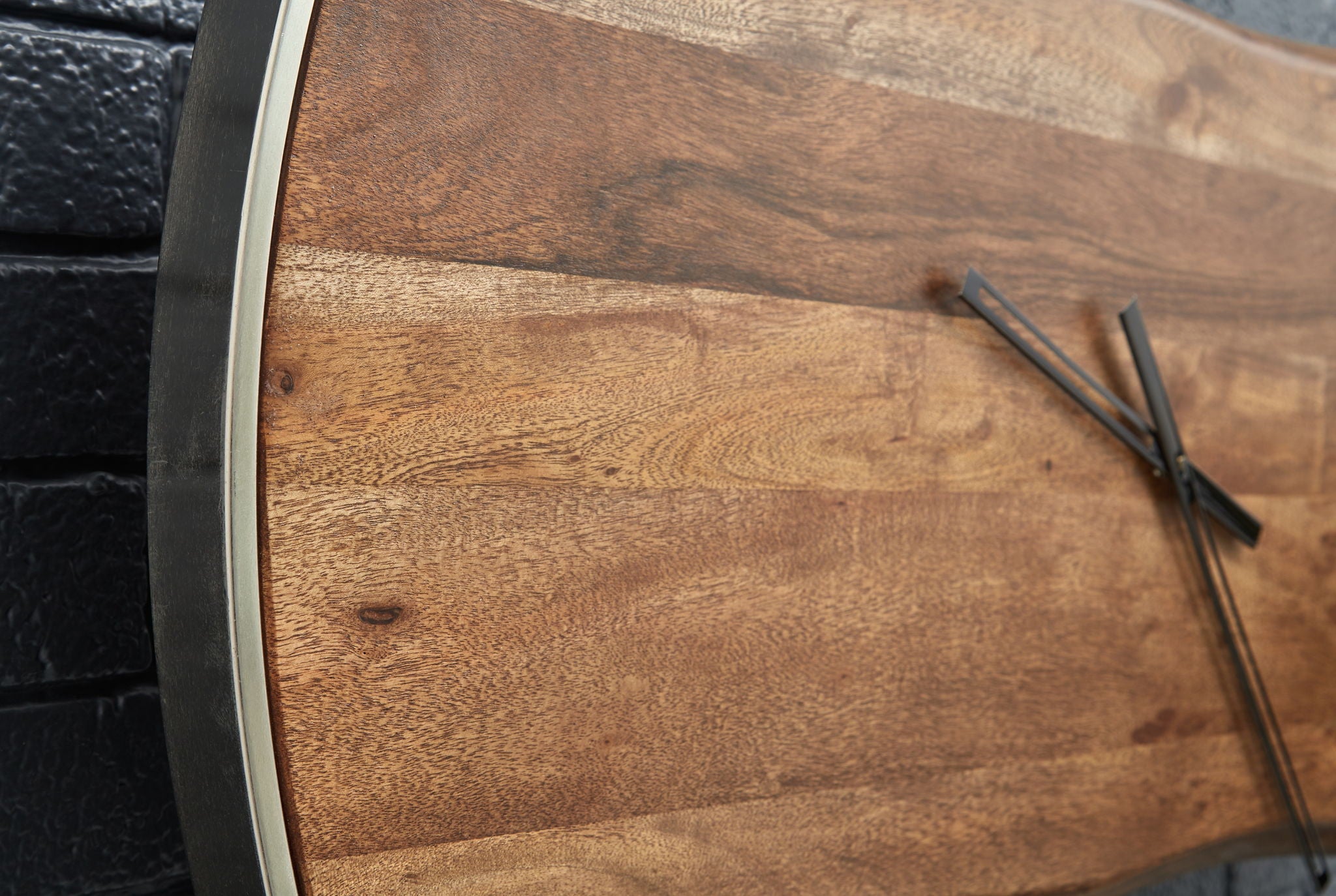 Close-up of brown wood-grain wall clock face with black hands and silver bezel