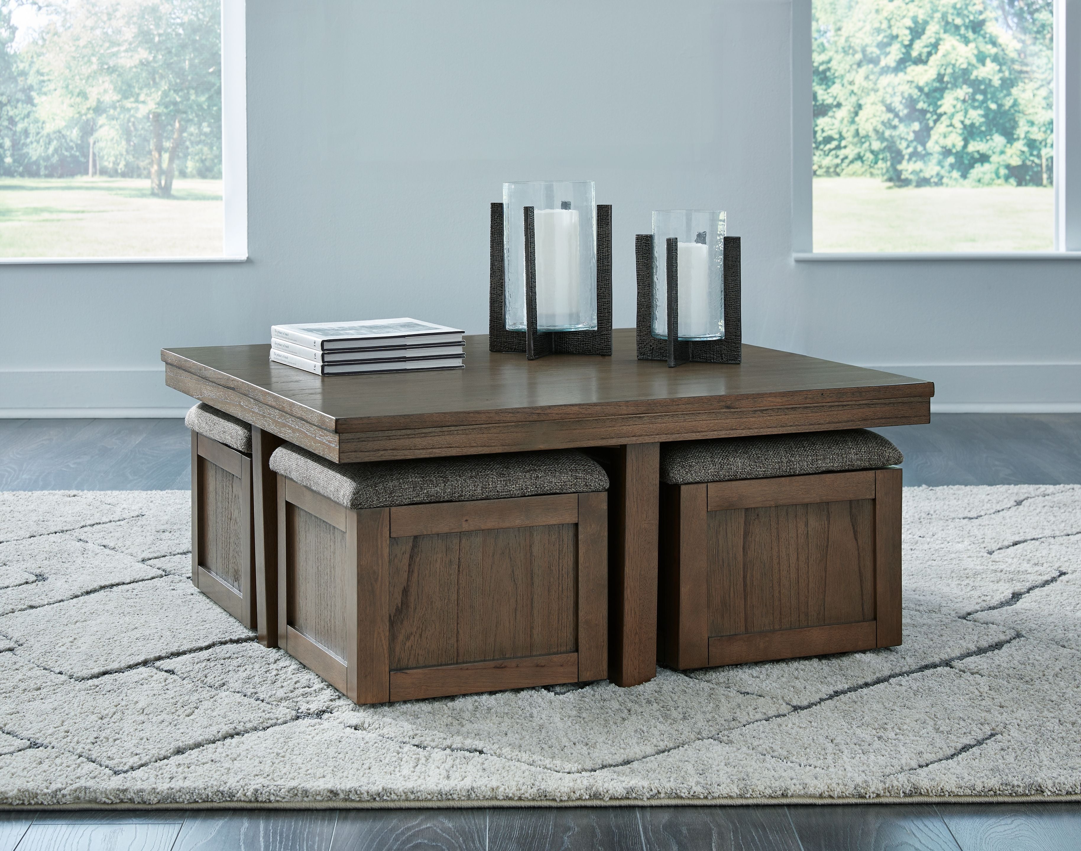 Brown cocktail table with two gray upholstered stools, paneled wood sides and legs.