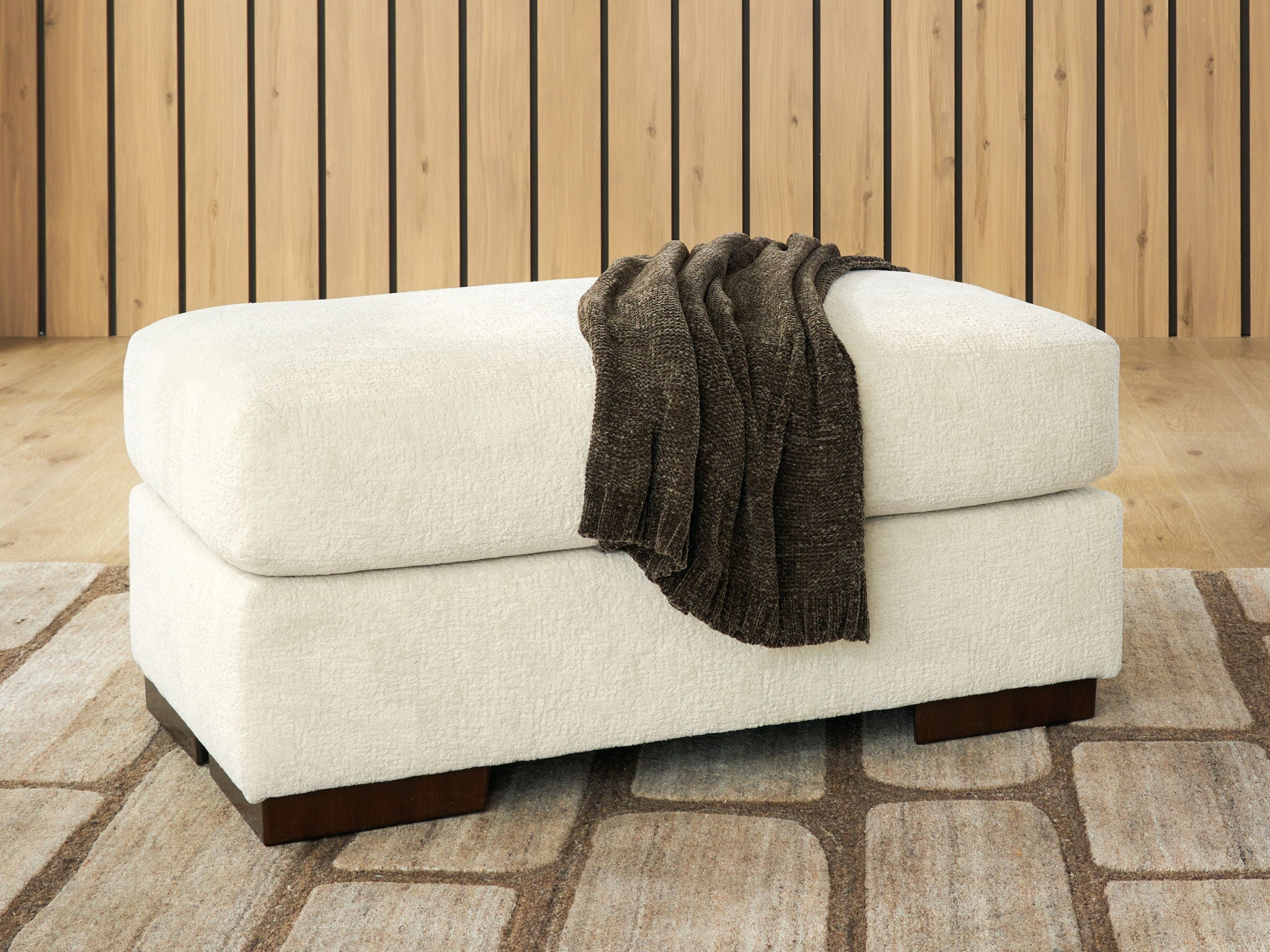 White fabric ottoman with dark legs and gray throw draped on top.