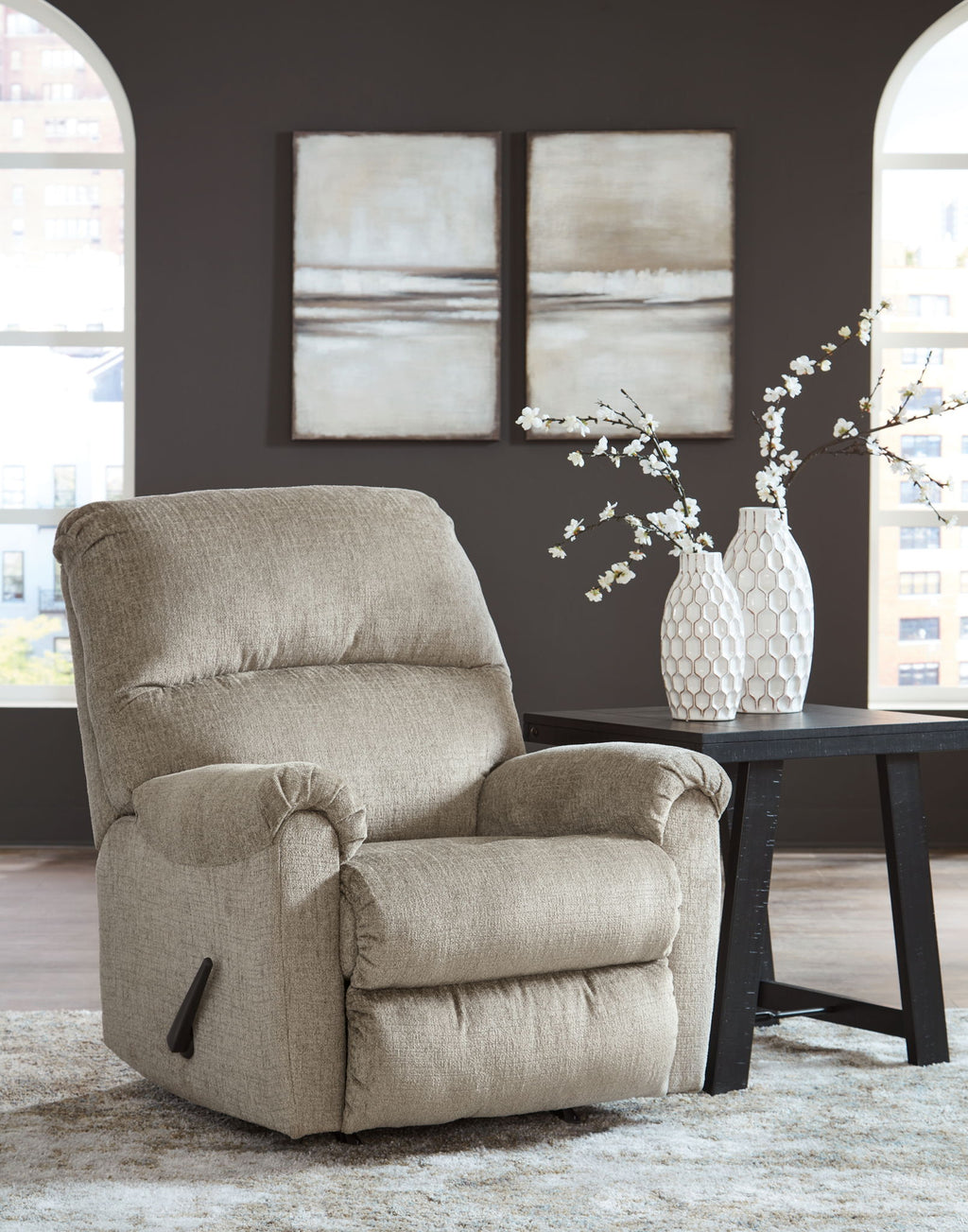 Taupe rocker recliner chair with padded headrest and armrests in a living room