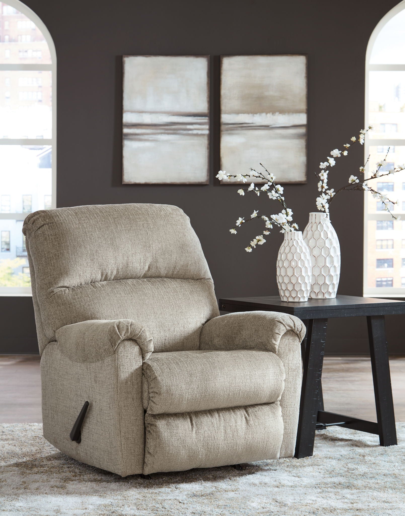 Taupe rocker recliner chair with padded headrest and armrests in a living room