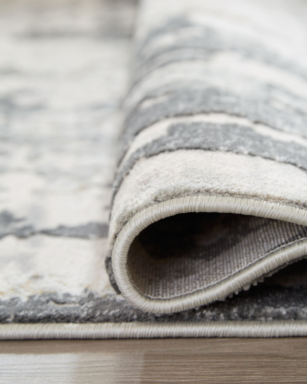 Rolled gray area rug edge showing low pile and stitched binding