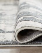 Rolled gray area rug edge showing low pile and stitched binding