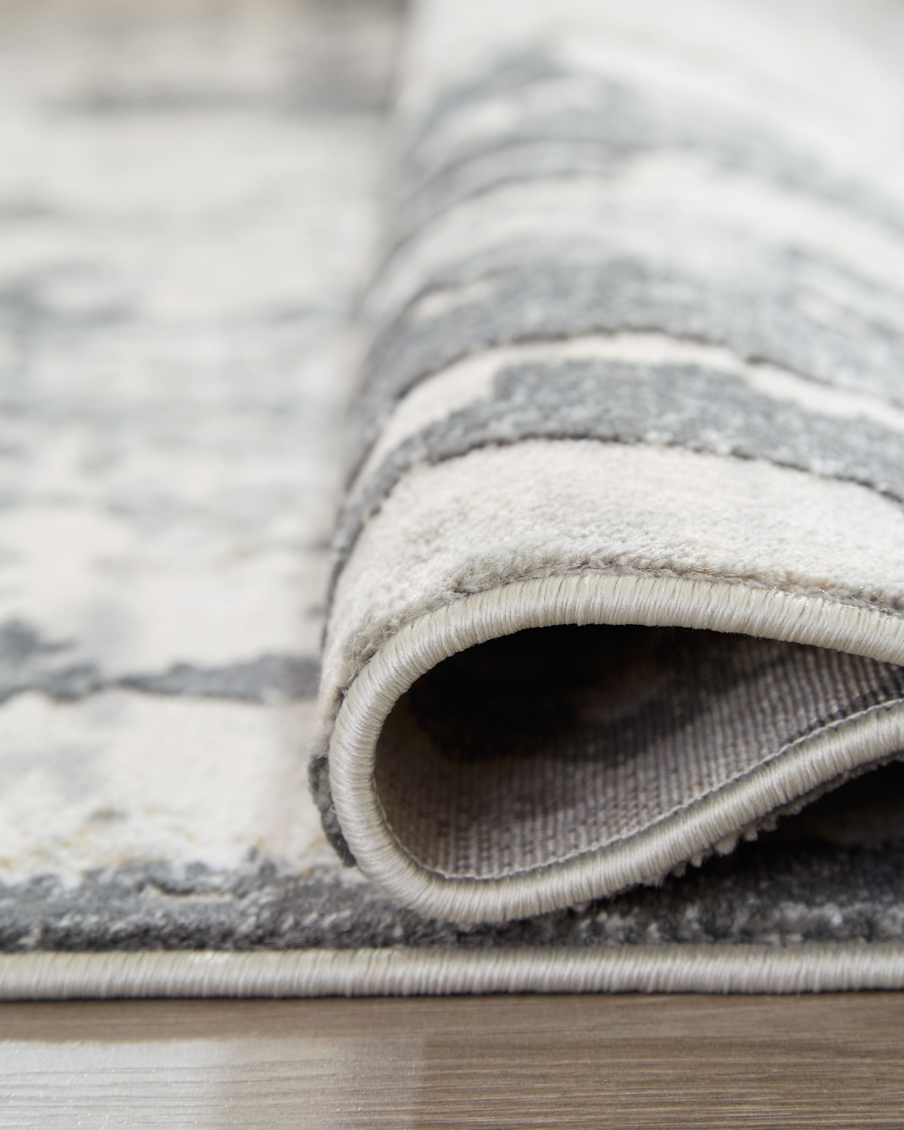 Rolled gray area rug edge showing low pile and stitched binding