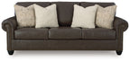 Dark brown upholstered sofa with three seats and two patterned accent pillows.