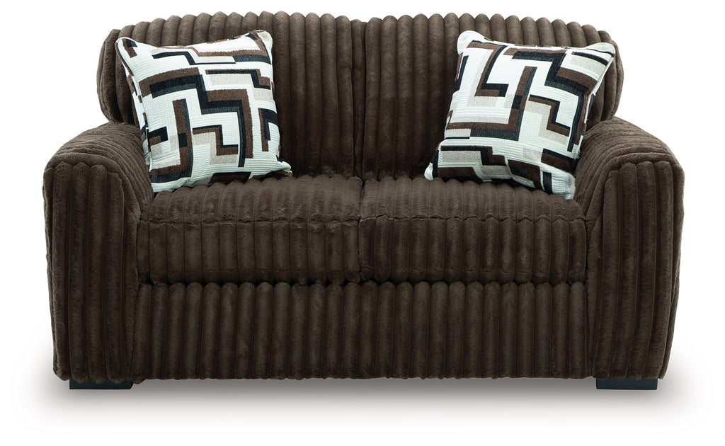 Dark brown loveseat with two geometric throw pillows and tufted front cushion