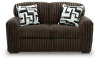 Dark brown loveseat with two geometric throw pillows and tufted front cushion
