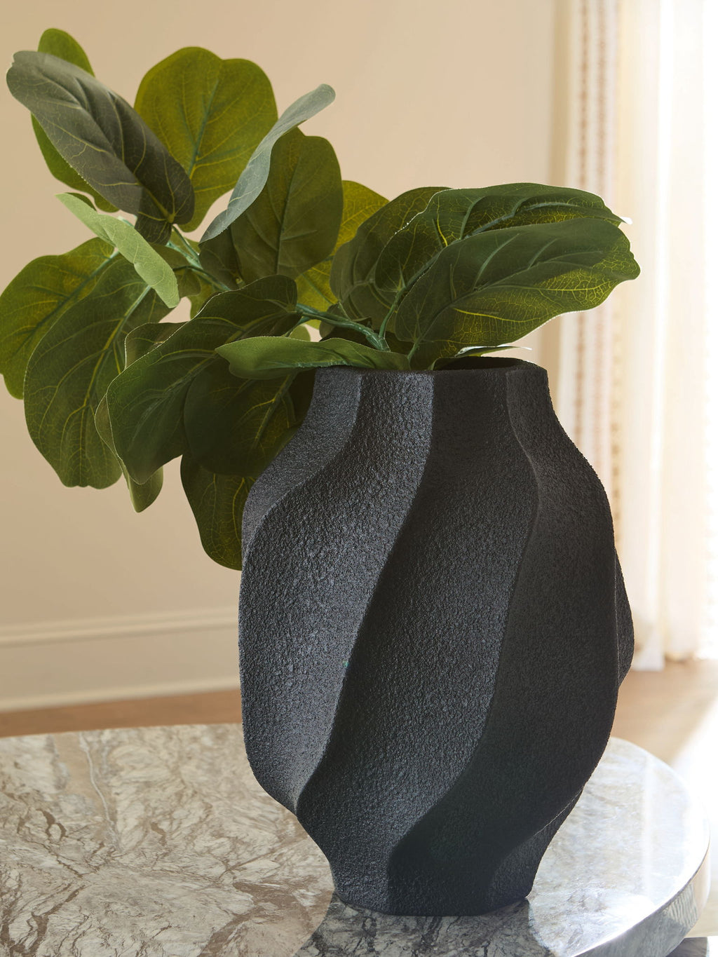 Black textured vase holding green leaves, fluted sides and round opening