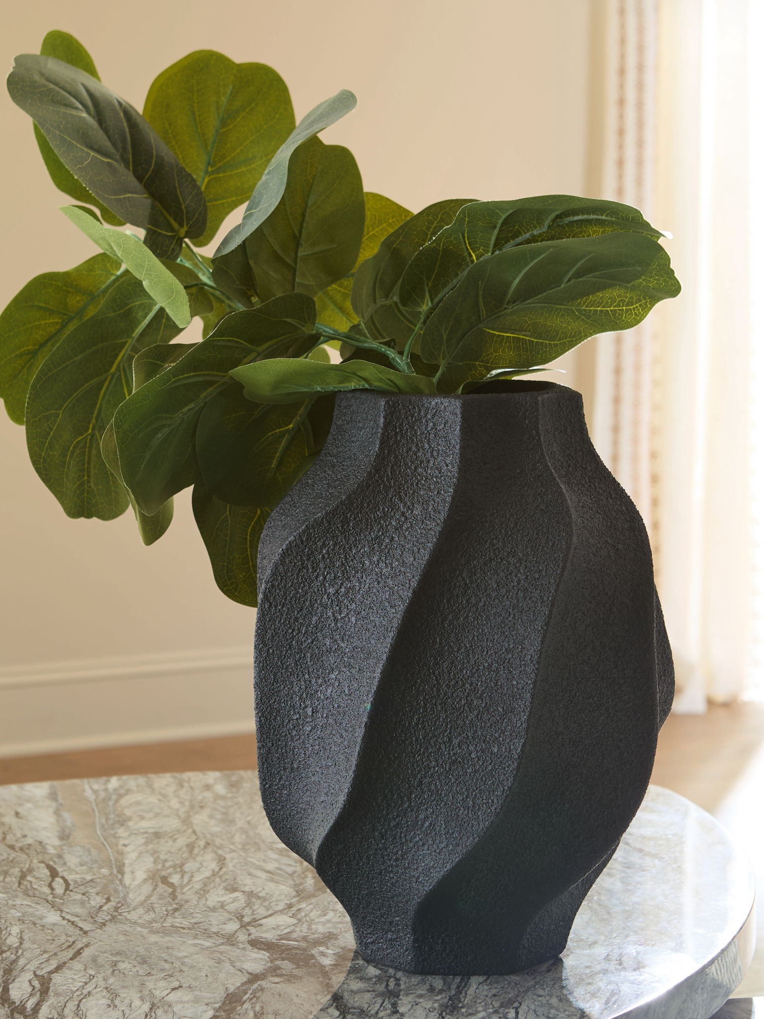 Black textured vase holding green leaves, fluted sides and round opening