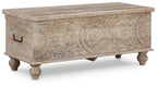 Beige storage bench with carved front panel, black handle, and turned wooden legs