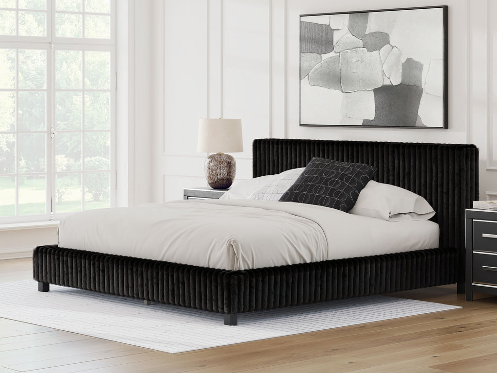 Black upholstered bed with tall headboard, low platform frame, and pillows on top.