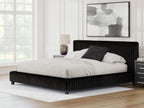 Black upholstered bed with tall headboard, low platform frame, and pillows on top.