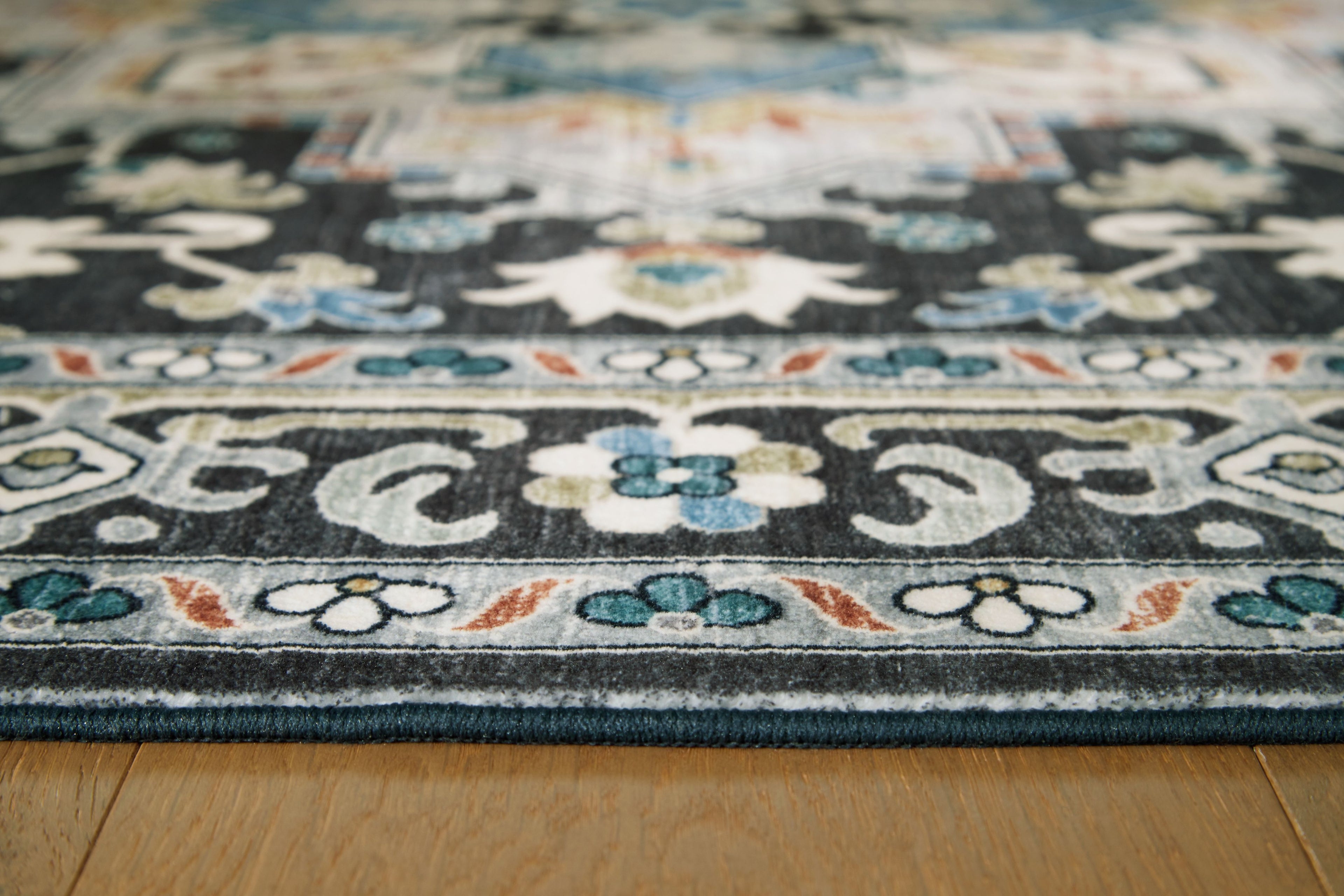 Washable area rug border close-up with black ground and light blue floral accents.