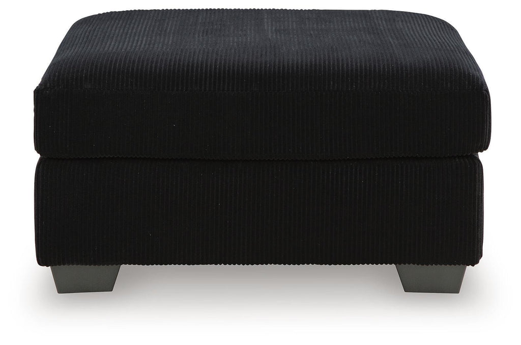 Black oversized ottoman with ribbed fabric, rounded padded top, dark legs.