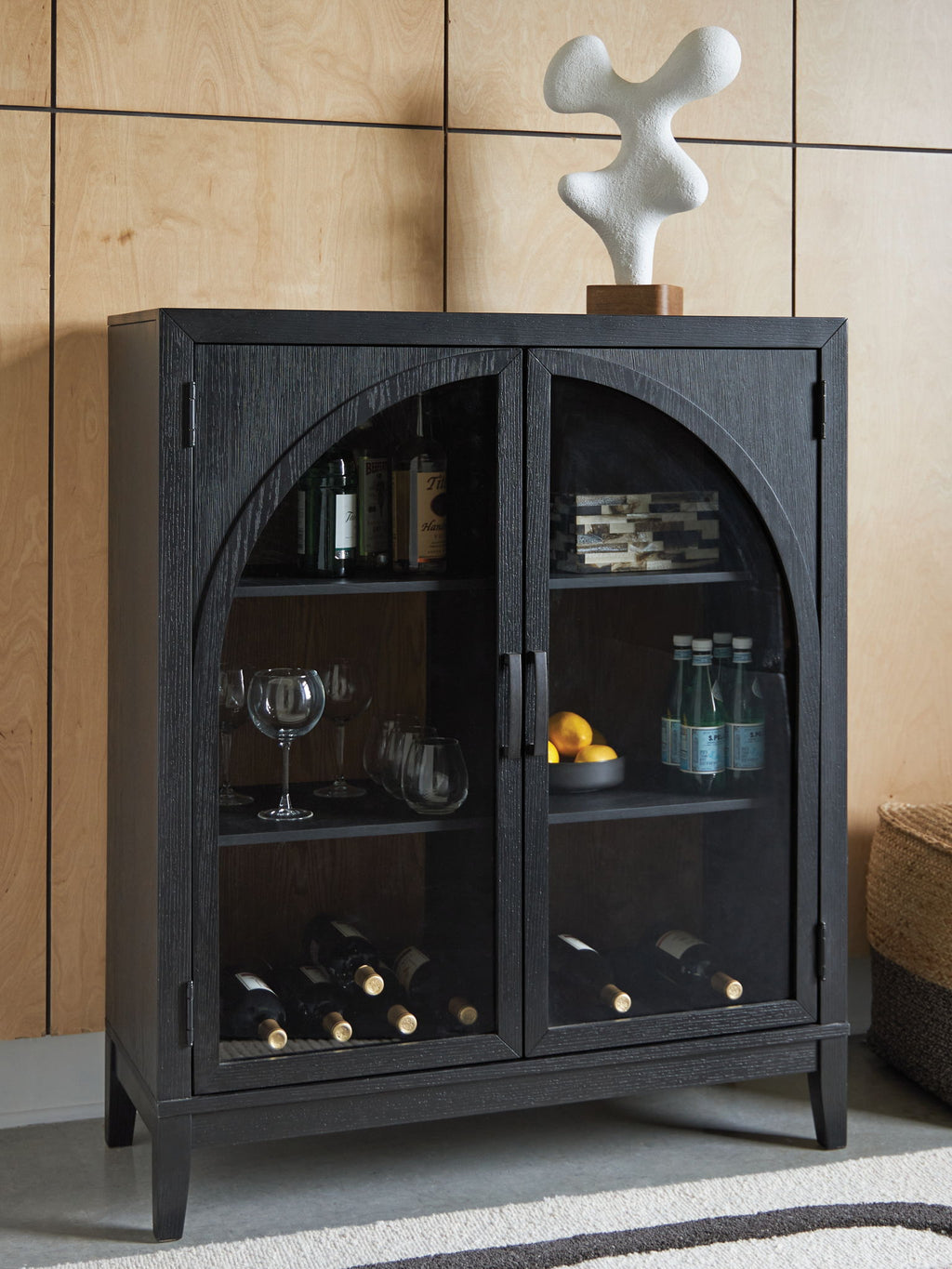 Black bar cabinet with arched glass doors showing bottles, stemware, and wine storage