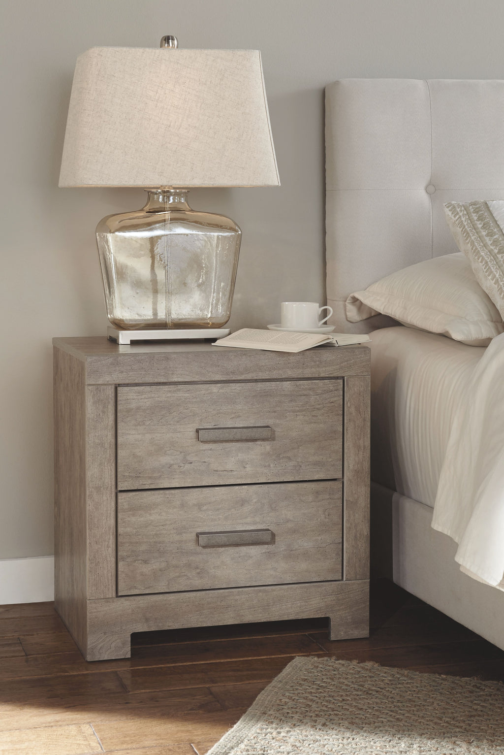 Gray nightstand with two drawers, table lamp, and folded linens