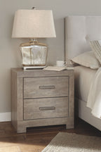 Gray nightstand with two drawers, table lamp, and folded linens