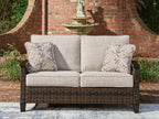 Dark brown wicker loveseat with beige cushions and two leaf-pattern throw pillows