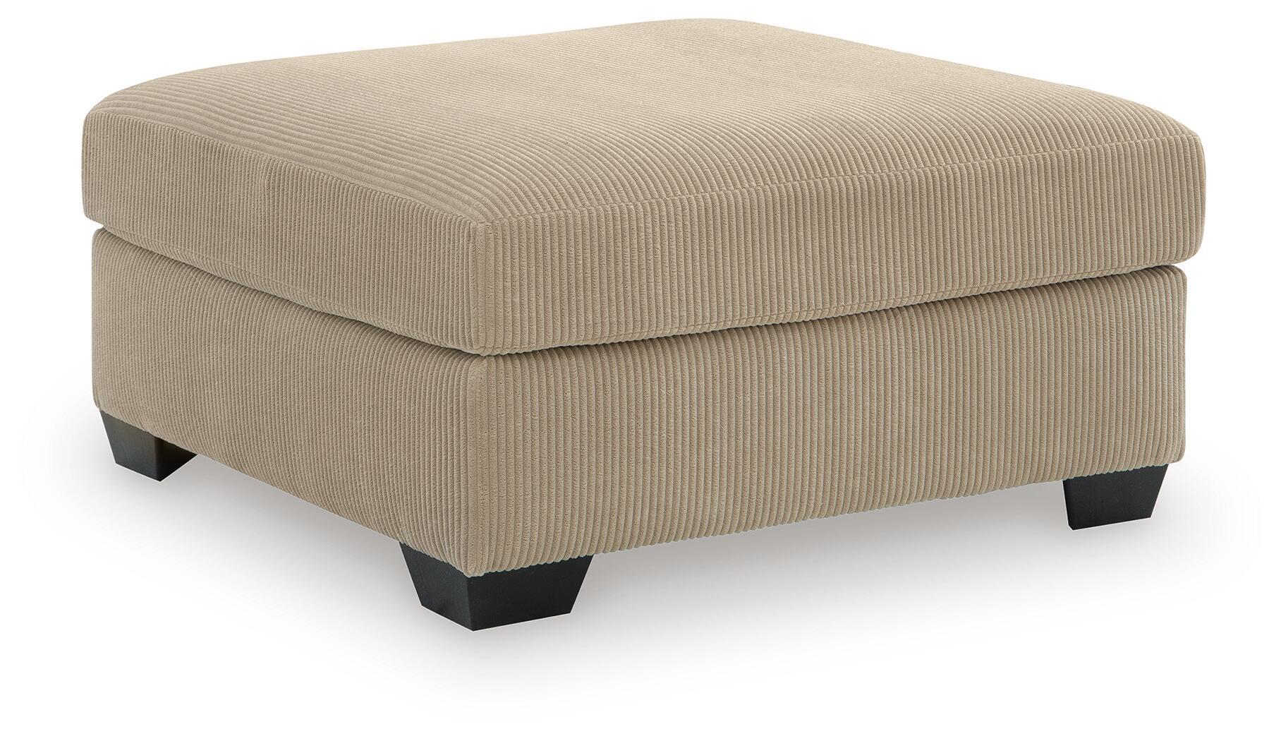 Beige oversized ottoman with ribbed fabric, square padded top, dark legs.