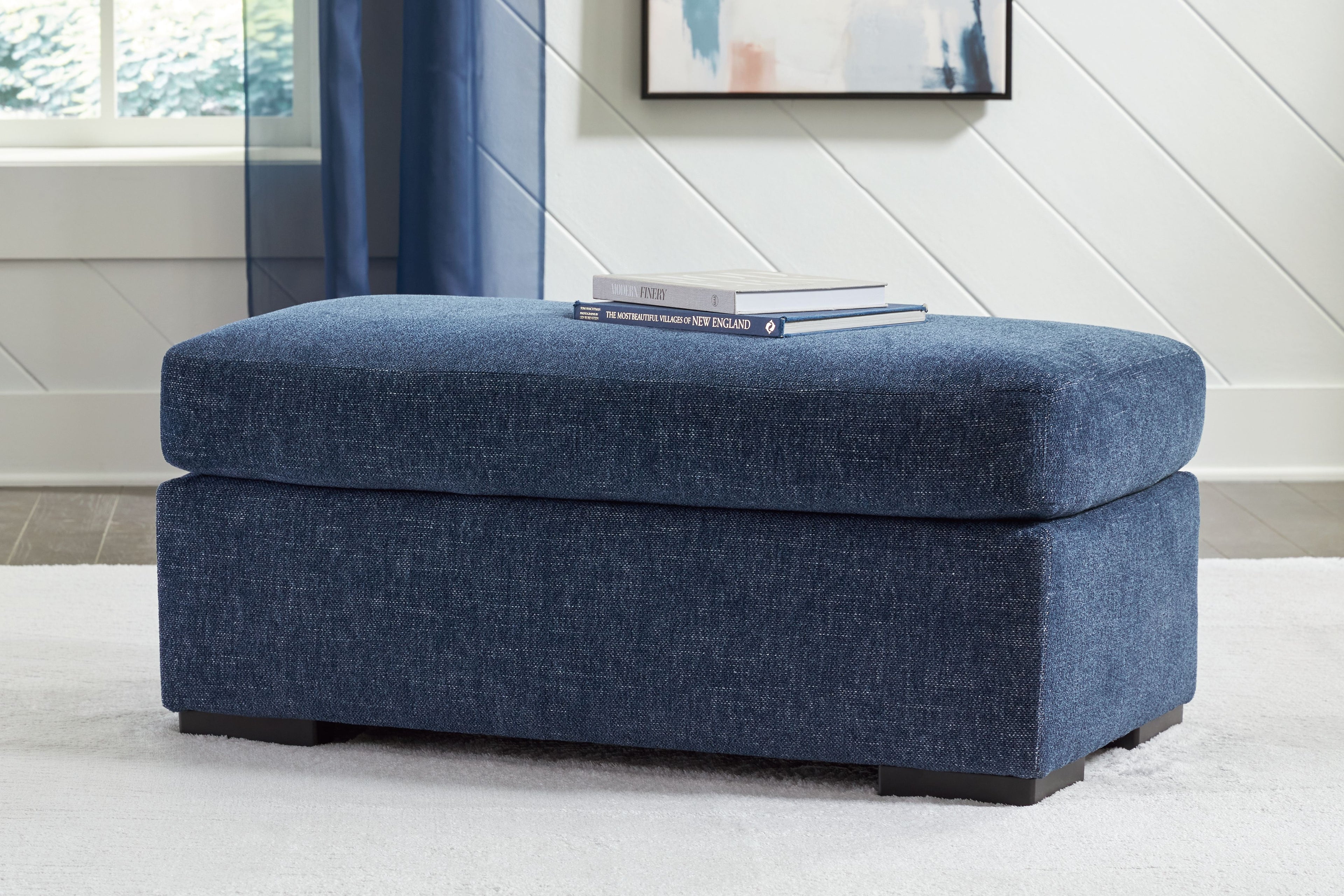 Blue upholstered ottoman with thick cushioned top and dark legs
