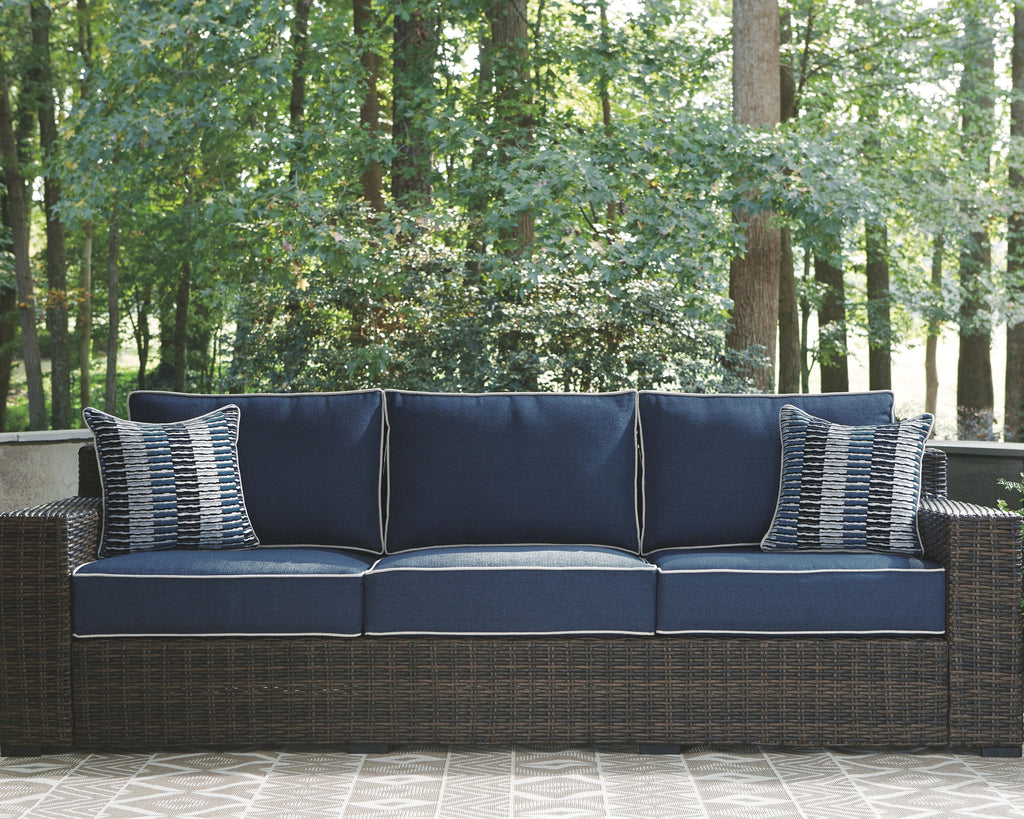 Brown wicker sofa with blue seat and back cushions and two striped accent pillows