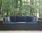 Brown wicker sofa with blue seat and back cushions and two striped accent pillows