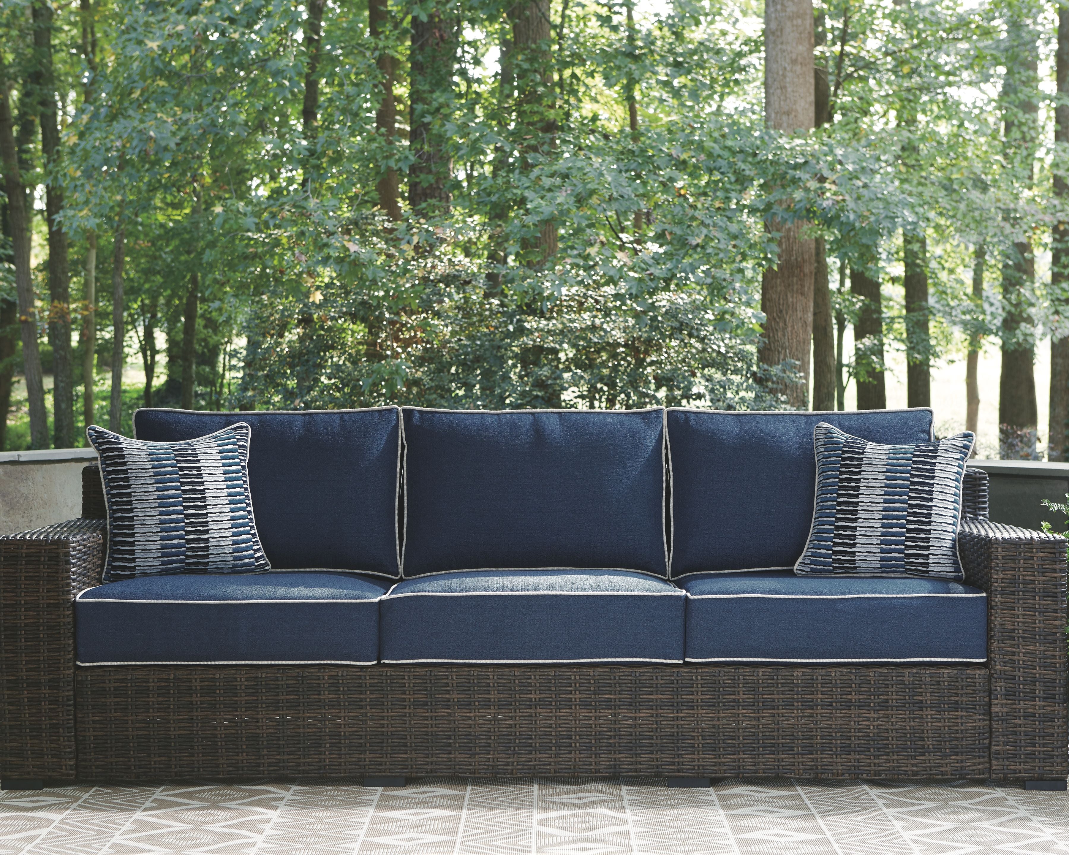 Brown wicker sofa with blue seat and back cushions and two striped accent pillows