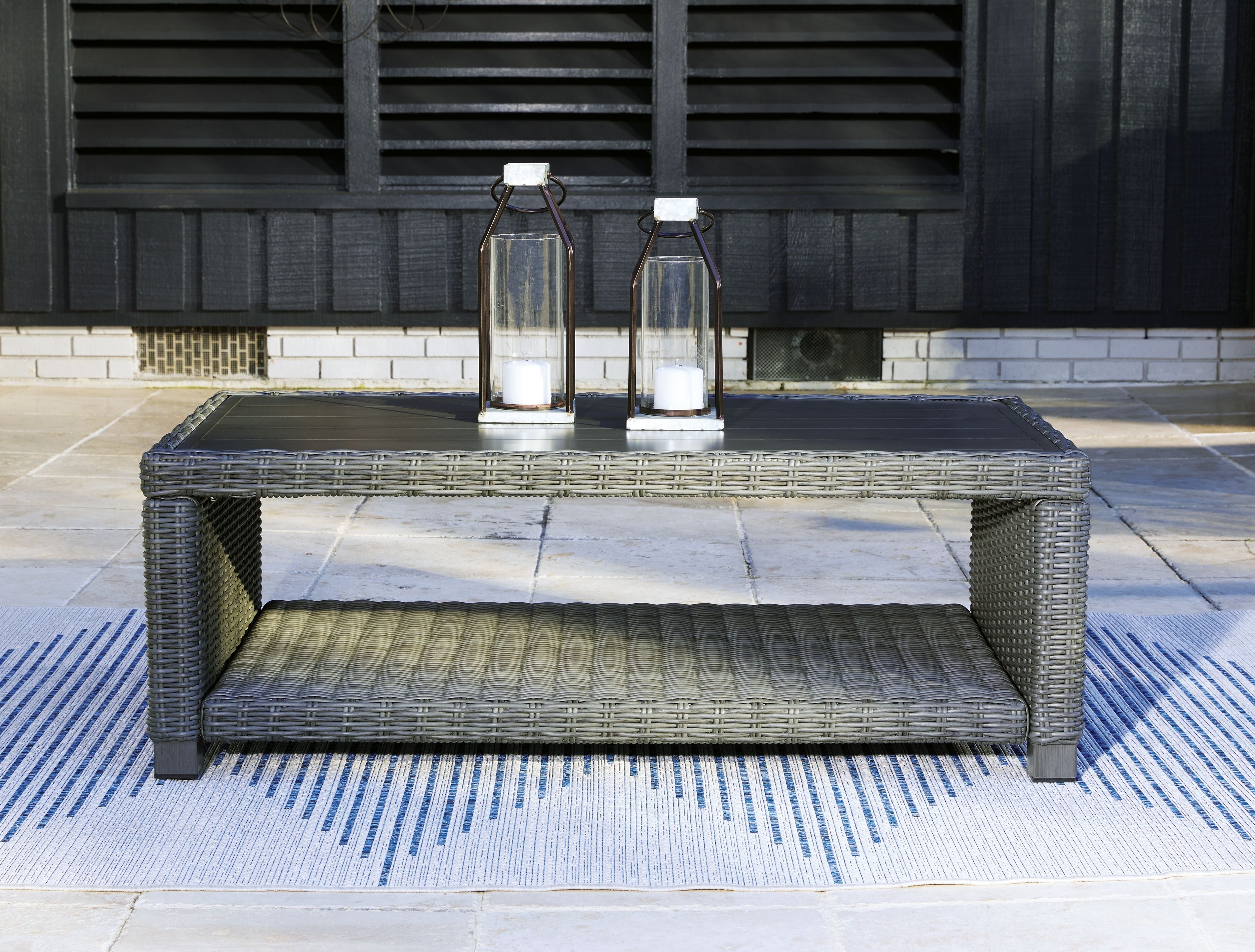 Gray rectangular cocktail table with woven frame and gray cushion shelf