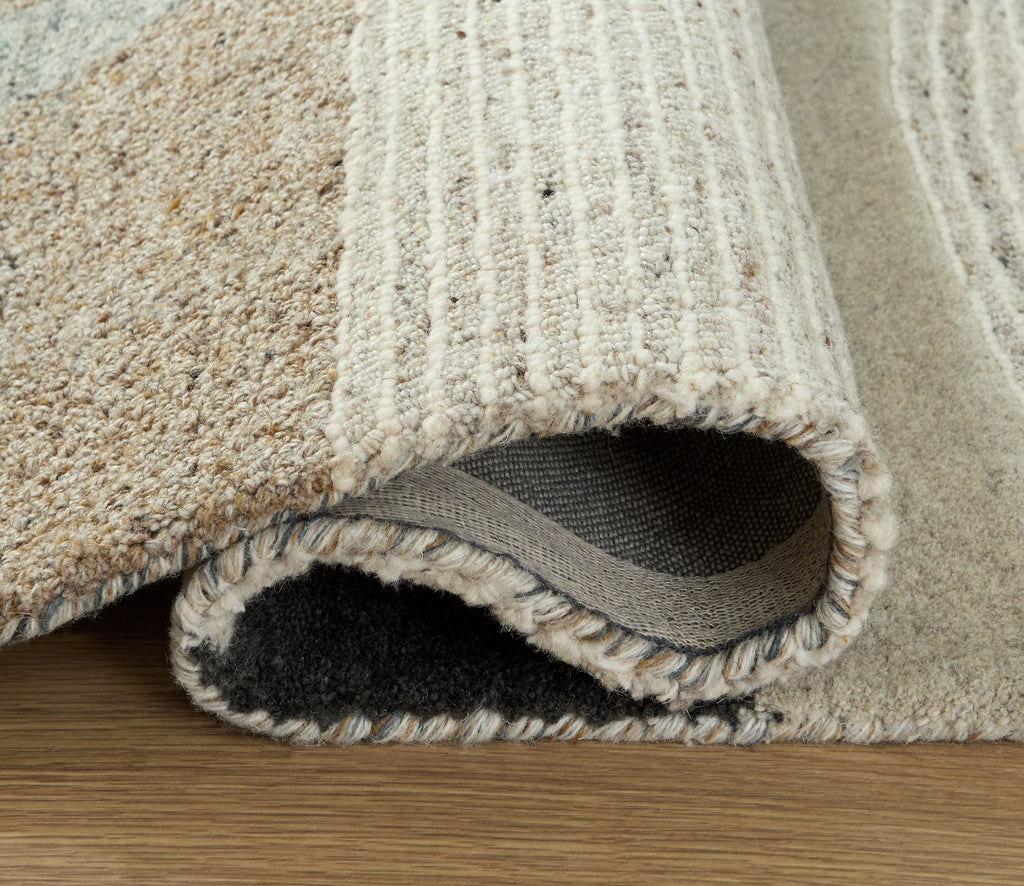 Beige area rug edge with short fringe and visible backing; textured looped fibers along border