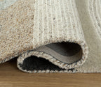 Beige area rug edge with short fringe and visible backing; textured looped fibers along border